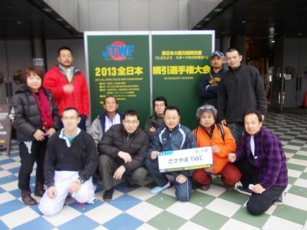 2013全日本綱引選手権大会と書かれた看板の前でジャージを着た11名の参加者が並んで記念撮影している写真